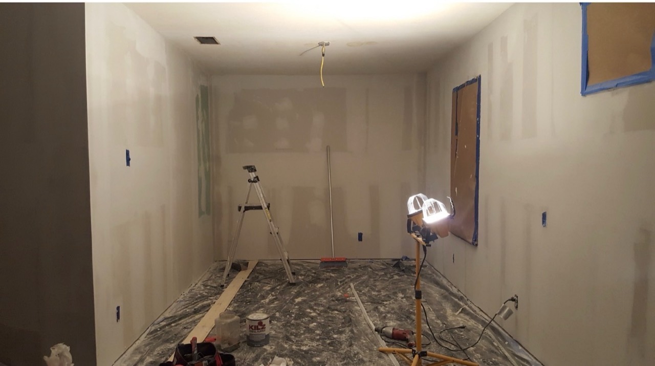 Room with unfinished drywall, covered floors, and work lights