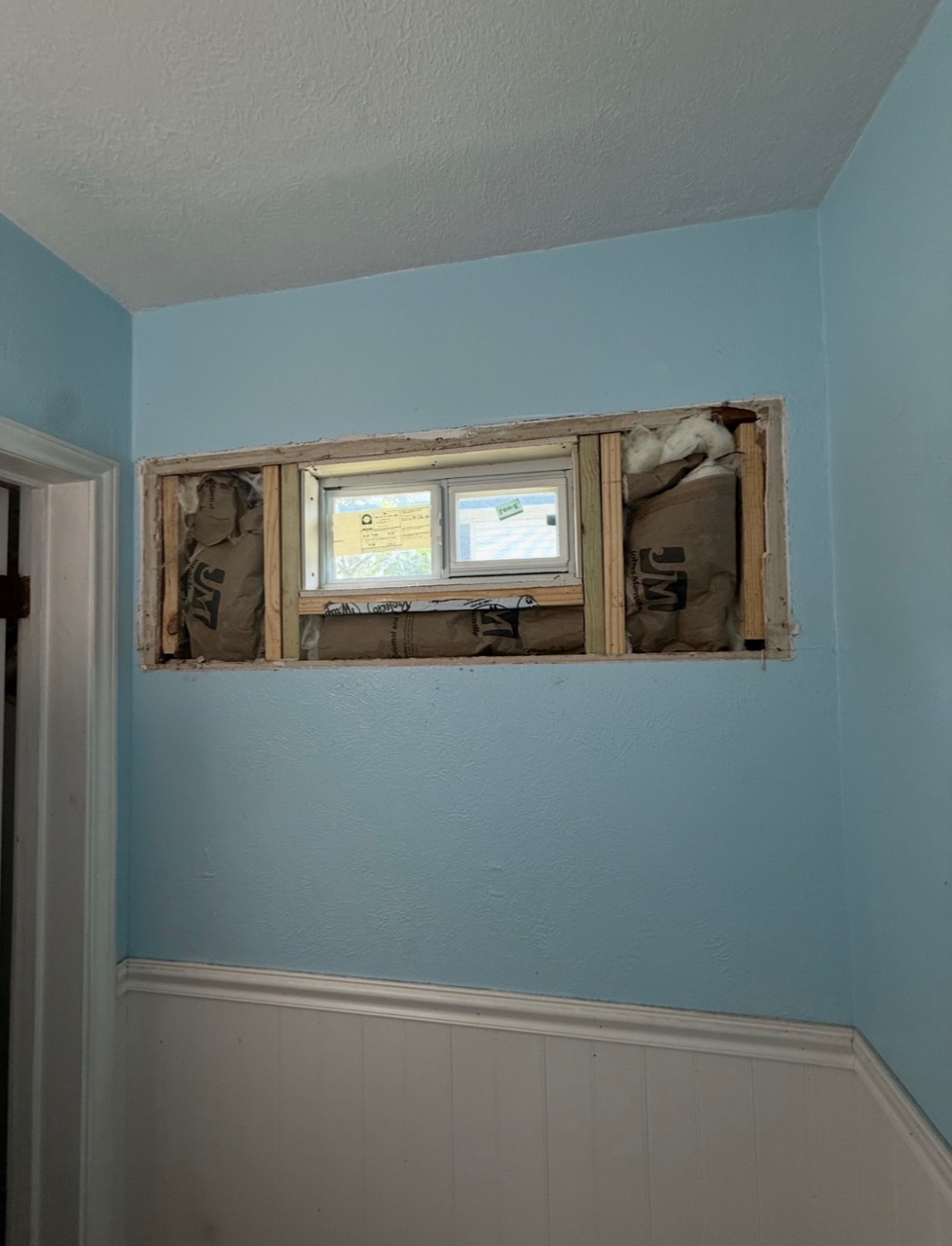 Exposed framing and insulation around a small bathroom window